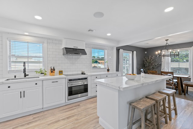 44 Williams St, Stonington, CT 06379 - kitchen featuring oven, wall chimney range hood, black electric stovetop, a breakfast bar, and light wood-type flooring