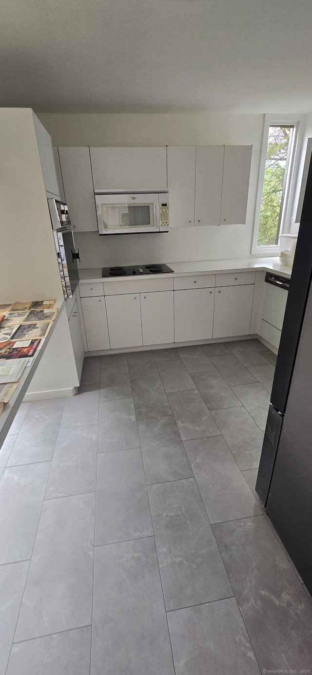 100 Mildred Ave, Waterbury, CT 06708 - kitchen with white microwave, black electric stovetop, light countertops, white cabinets, and freestanding refrigerator