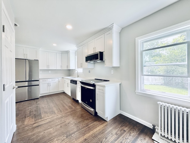 10 Meadowpark Ave W, Stamford, CT 06905 - kitchen featuring appliances with stainless steel finishes, radiator heating unit, dark wood-type flooring, white cabinets, and light countertops