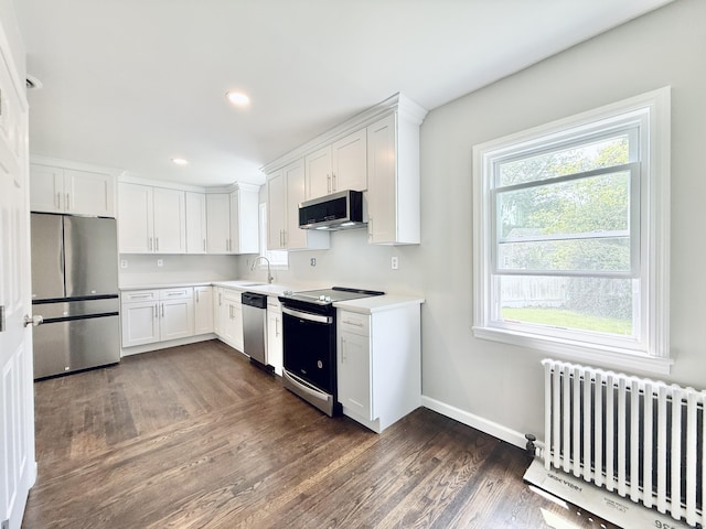 10 Meadowpark Ave W, Stamford, CT 06905 - kitchen featuring appliances with stainless steel finishes, radiator heating unit, dark wood-type flooring, white cabinetry, and light countertops