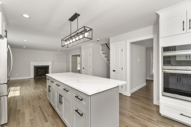 61 N Woods Rd, Hamden, CT 06518 - kitchen with stainless steel appliances, open floor plan, a center island, wood finished floors, and white cabinets