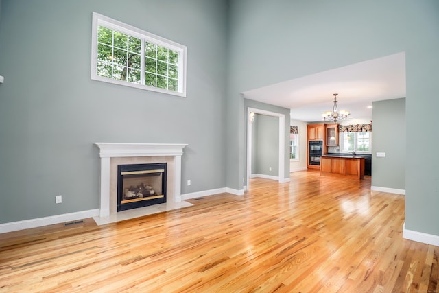 21 Great Heron Ln Unit 21, Brookfield, CT 06804 - unfurnished living room featuring a tile fireplace, light wood-type flooring, a chandelier, and a towering ceiling