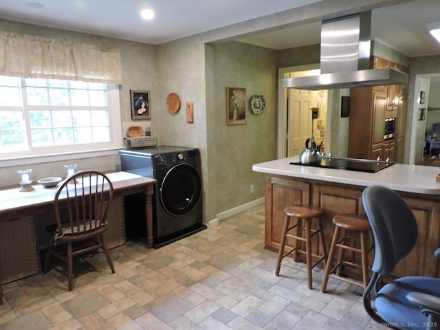 29 Graham Rd, East Windsor, CT 06016 - kitchen with wall chimney exhaust hood, black electric cooktop, washer / dryer, a breakfast bar area, and light countertops