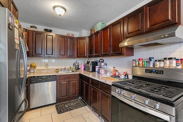 11 Bedford Ave Apt J2, Norwalk, CT 06850 - kitchen with stainless steel appliances, under cabinet range hood, backsplash, light tile patterned floors, and light stone counters