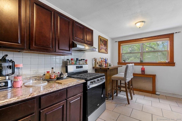 11 Bedford Ave Apt J2, Norwalk, CT 06850 - kitchen with stainless steel gas range, under cabinet range hood, decorative backsplash, light tile patterned flooring, and dark brown cabinets