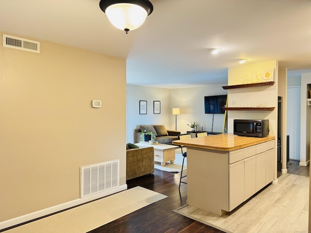 110 Trolley Crossing Ln Unit 110, Middletown, CT 06457 - kitchen featuring white cabinets, wood finished floors, a kitchen breakfast bar, black microwave, and open shelves