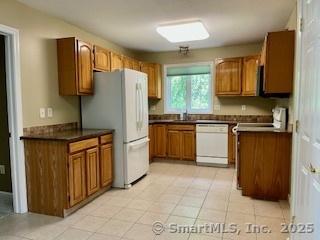 1929 Logans Way, Windsor, CT 06095 - kitchen featuring brown cabinets, white appliances, dark countertops, and light tile patterned floors