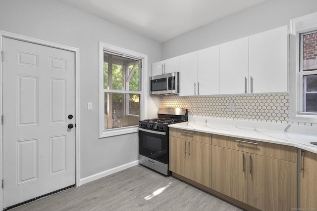 276 Bond St, Bridgeport, CT 06610 - kitchen featuring stainless steel appliances, light stone countertops, decorative backsplash, light wood finished floors, and white cabinets