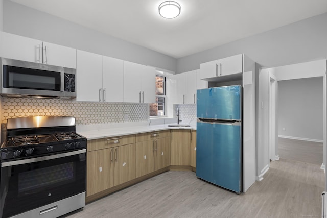 276 Bond St, Bridgeport, CT 06610 - kitchen featuring appliances with stainless steel finishes, light wood-style flooring, tasteful backsplash, and white cabinetry