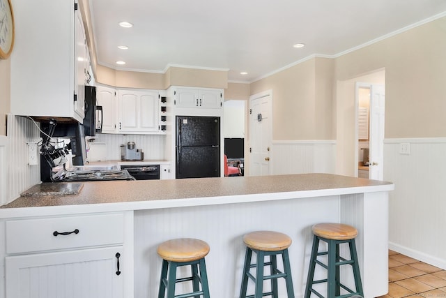 35 Pheasant Ln, Ridgefield, CT 06877 - kitchen featuring black appliances, a peninsula, wainscoting, a kitchen bar, and white cabinets