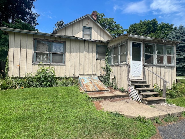 130 Wilkins Ave, Bridgeport, CT 06606 - view of front of house with board and batten siding, a chimney, a front lawn, and a sunroom