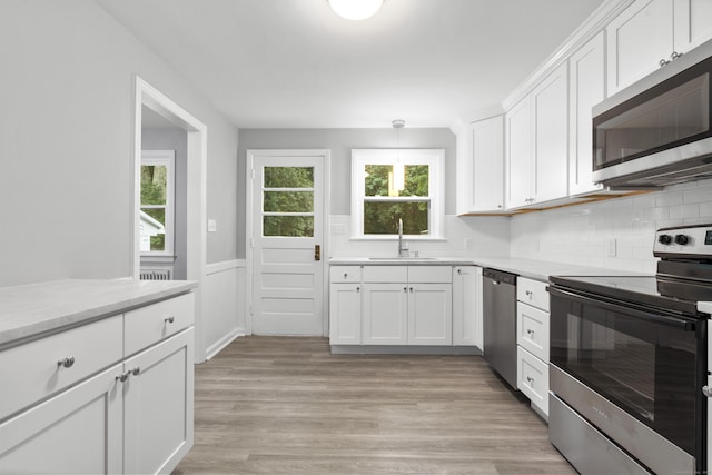 106 Lakeview Ave, West Haven, CT 06516 - kitchen with stainless steel appliances, white cabinetry, wainscoting, tasteful backsplash, and light wood-style flooring