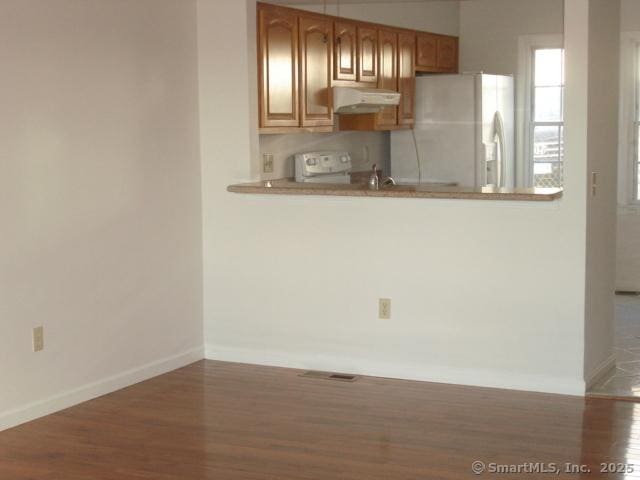 55 Mill Plain Rd Unit 17-6, Danbury, CT 06811 - kitchen featuring wood finished floors, white fridge with ice dispenser, under cabinet range hood, a peninsula, and light countertops