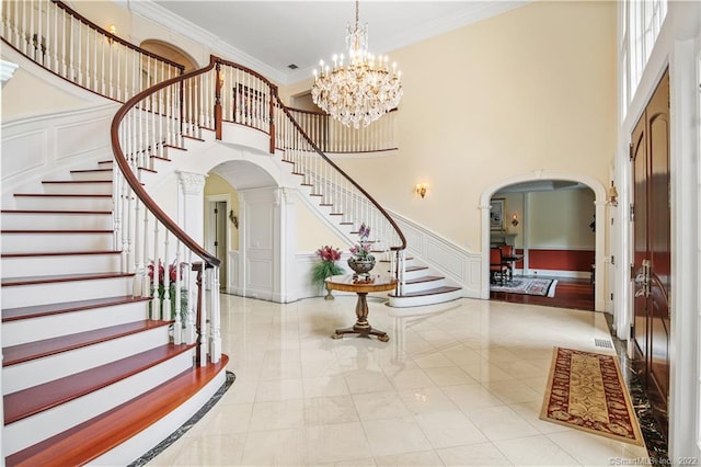 stairway featuring a towering ceiling, crown molding, a notable chandelier, and light hardwood / wood-style flooring