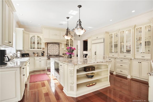 kitchen featuring built in appliances, pendant lighting, light stone counters, dark wood-type flooring, and a center island