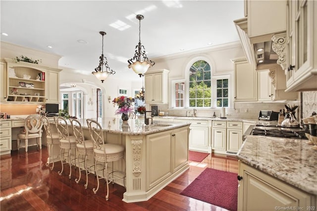 kitchen featuring dark hardwood / wood-style flooring, backsplash, a breakfast bar area, an island with sink, and cream cabinetry