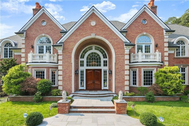 view of front facade with a front yard, french doors, and a balcony