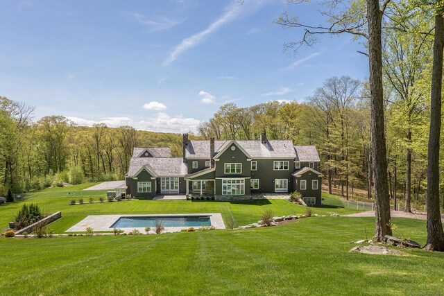 rear view of property with a wooded view, a lawn, an outdoor pool, and a chimney