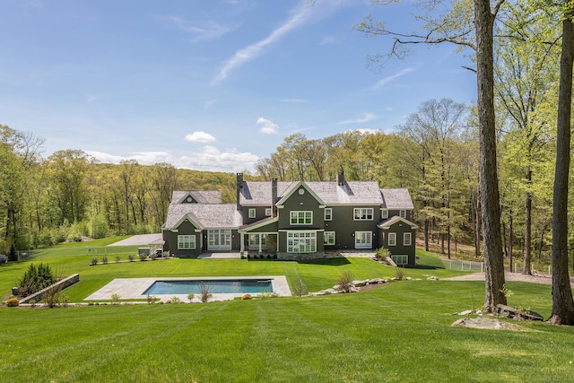 rear view of property with an outdoor pool, a patio, a view of trees, and a lawn