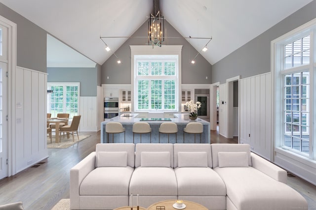 living area featuring visible vents, wainscoting, an inviting chandelier, wood finished floors, and high vaulted ceiling