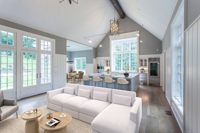 living room featuring dark wood-type flooring, beamed ceiling, a notable chandelier, and plenty of natural light