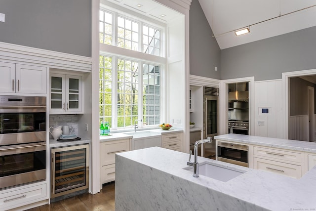 kitchen featuring a sink, stainless steel appliances, light stone counters, and beverage cooler