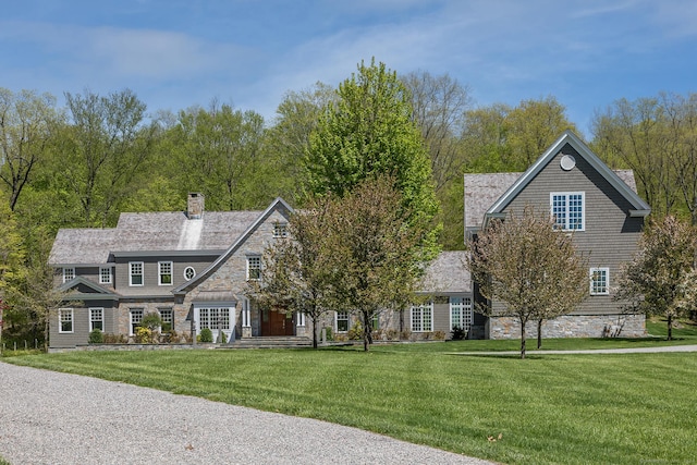 shingle-style home featuring stone siding, a front lawn, and a chimney