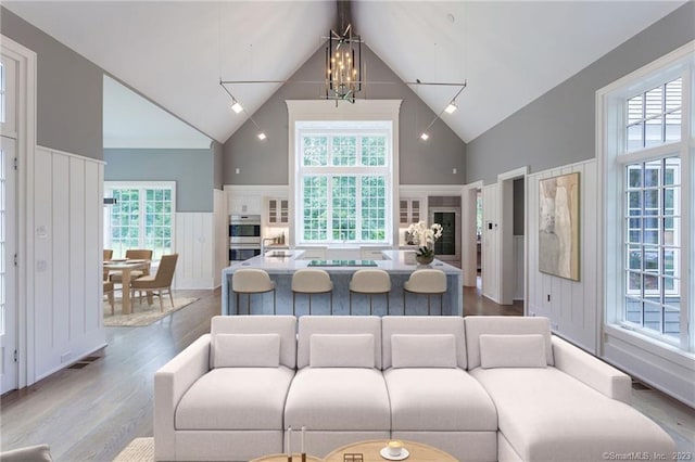 living room with wood finished floors, visible vents, a wainscoted wall, high vaulted ceiling, and a notable chandelier