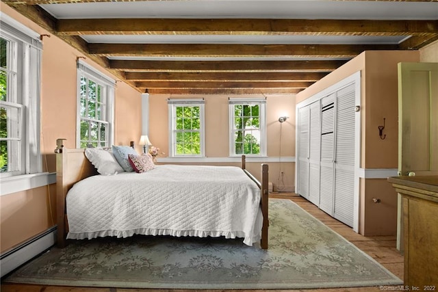 bedroom featuring light hardwood / wood-style floors, a closet, a baseboard heating unit, and beamed ceiling