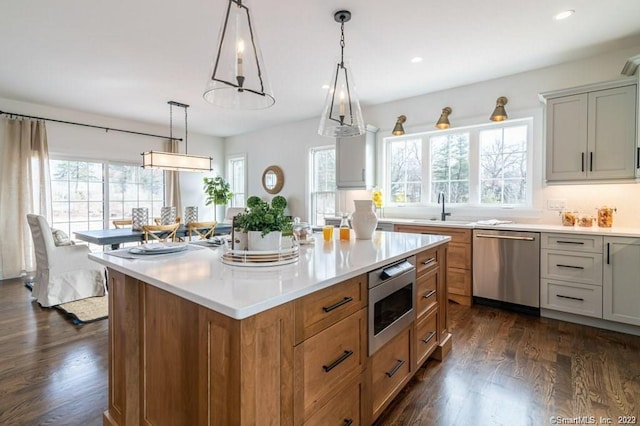 kitchen featuring stainless steel appliances, decorative light fixtures, dark hardwood / wood-style flooring, sink, and a center island with sink