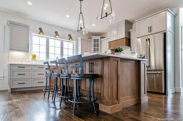 kitchen featuring hanging light fixtures, a center island, a breakfast bar area, dark hardwood / wood-style flooring, and high end fridge