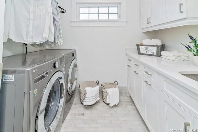 clothes washing area with light tile floors, washer and clothes dryer, and cabinets