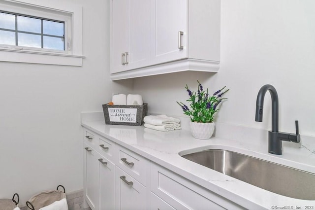 kitchen with white cabinetry, light stone counters, and sink