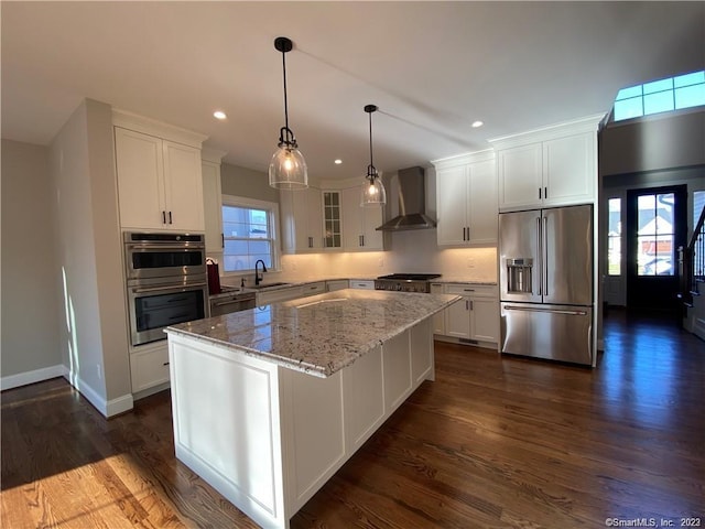 kitchen with dark hardwood / wood-style floors, wall chimney exhaust hood, a center island, and appliances with stainless steel finishes