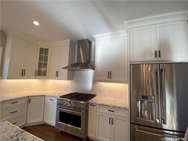 kitchen with high quality appliances, backsplash, white cabinets, and wall chimney range hood