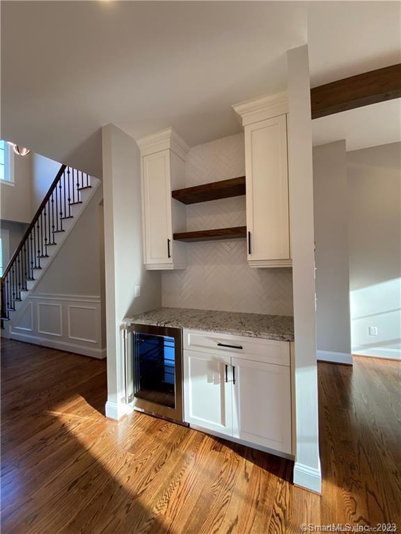 kitchen with dark wood-type flooring, light stone counters, backsplash, wine cooler, and white cabinetry