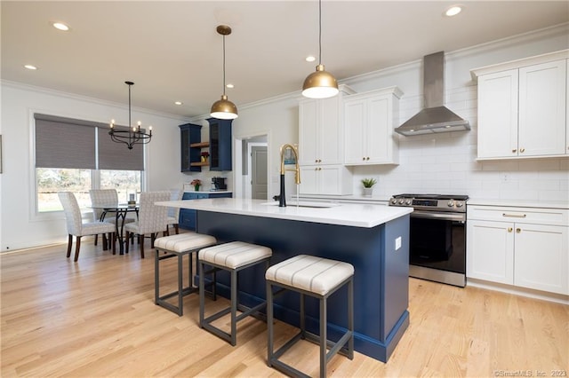 kitchen featuring an inviting chandelier, light hardwood / wood-style floors, an island with sink, stainless steel range, and wall chimney exhaust hood