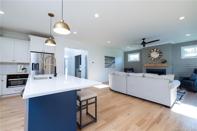 interior space with ceiling fan, a fireplace, sink, light hardwood / wood-style flooring, and ornamental molding