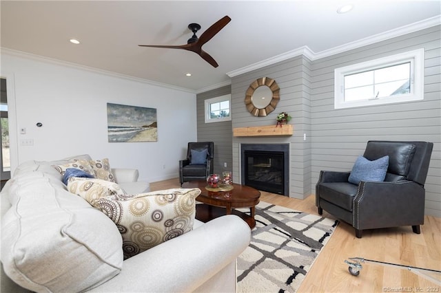 living room featuring ceiling fan, crown molding, a fireplace, wood walls, and light wood-type flooring