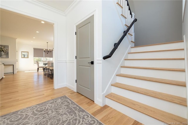 stairway featuring an inviting chandelier, crown molding, and light wood-type flooring