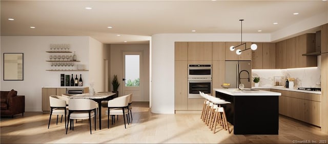 kitchen with a kitchen island with sink, sink, a chandelier, stainless steel appliances, and decorative light fixtures