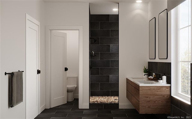 bathroom with tile flooring, toilet, a tile shower, and vanity