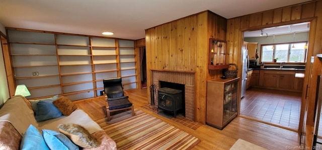 interior space featuring a wood stove, wooden walls, a fireplace, sink, and light hardwood / wood-style flooring