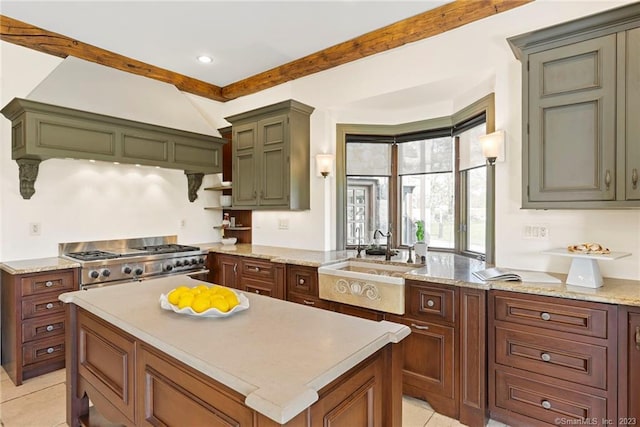 kitchen with light stone counters, a kitchen island, stainless steel range, sink, and light tile flooring