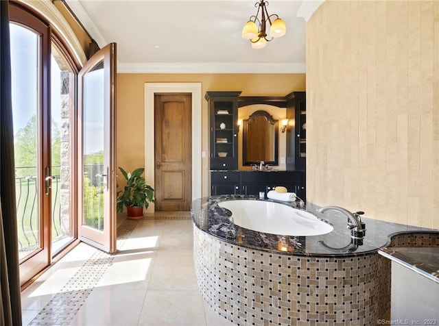 bathroom featuring a notable chandelier, vanity, ornamental molding, tile floors, and tiled tub