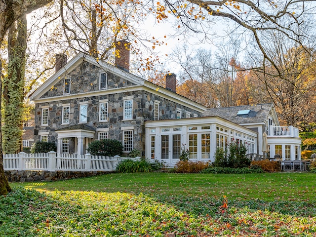 back of property featuring a balcony, a lawn, and a sunroom