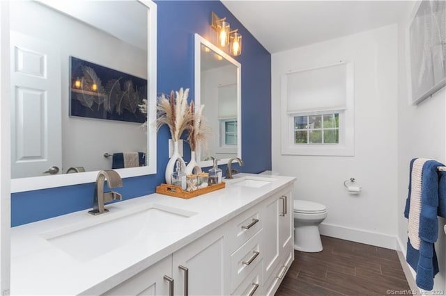 bathroom featuring toilet, vanity with extensive cabinet space, double sink, and wood-type flooring