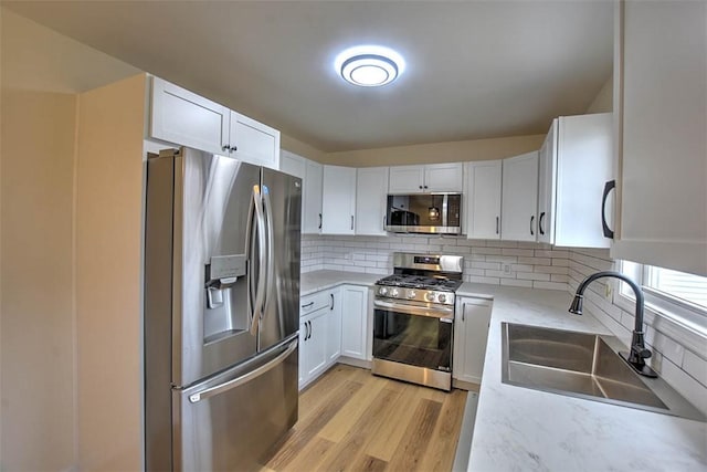 kitchen featuring sink, decorative backsplash, light wood-type flooring, white cabinetry, and stainless steel appliances