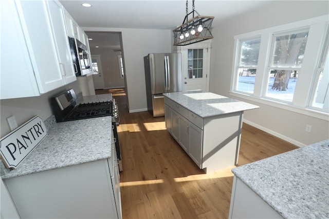 kitchen featuring pendant lighting, appliances with stainless steel finishes, white cabinetry, light stone counters, and a kitchen island