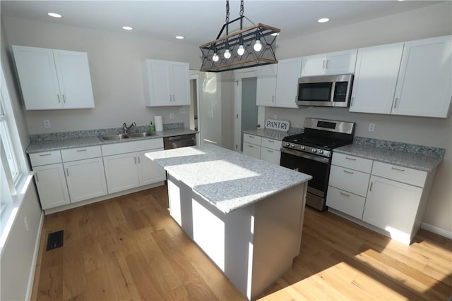 kitchen featuring stainless steel appliances, sink, white cabinets, a center island, and hanging light fixtures